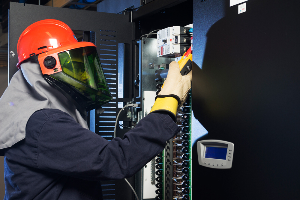 Data center service technician wearing PPE and performing UPS maintenance
